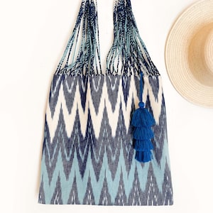 Op de afbeelding: Een blauwe en witte tote bag met ikat-patroon en een blauwe kwast. De tas heeft een geweven handvat en is gemaakt van een zachte, textuurrijke stof.