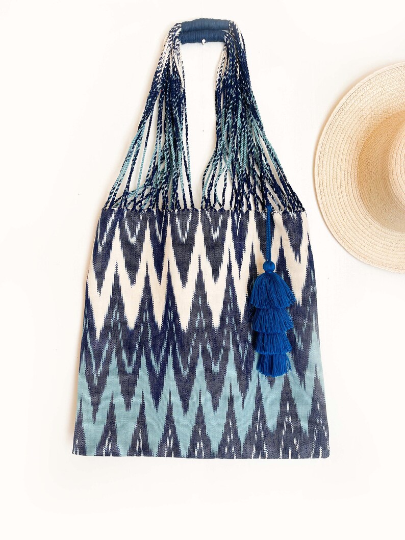 Op de afbeelding: Een blauwe en witte tote bag met ikat-patroon en een blauwe kwast. De tas heeft een geweven handvat en is gemaakt van een zachte, textuurrijke stof.