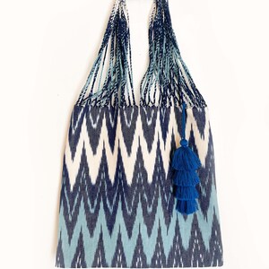 Op de afbeelding: Een blauwe en witte ikat tote bag met een blauwe kwast. De tas heeft een geweven ontwerp en een brede, stevige handvat.