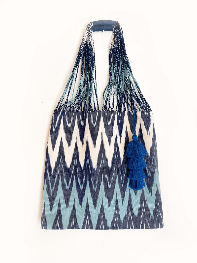 Op de afbeelding: Een blauwe en witte ikat tote bag met een blauwe kwast. De tas heeft een geweven ontwerp en een brede, stevige handvat.