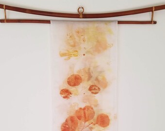 May include: A white fabric wall hanging with a brown bamboo rod at the top. The fabric has a pattern of orange and yellow leaf prints.