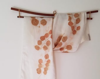 May include: A white silk scarf with a brown leaf pattern hanging on a wooden rod.