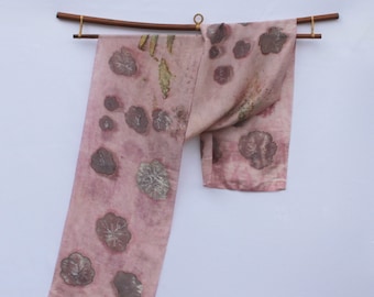 May include: A pink silk scarf with a floral pattern. The scarf is hanging on a wooden rod with gold accents.