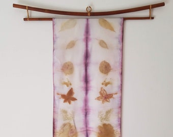 May include: A long, white silk scarf with a purple dye pattern and pressed leaves and flowers in shades of brown and tan.