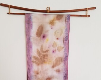 May include: A long, rectangular silk scarf with a pale pink and white background. The scarf is decorated with a pattern of brown leaves and flowers, and has a darker pink border.