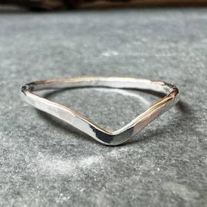 Può includere: Un semplice anello d'argento con un design a forma di V. L'anello è realizzato in metallo liscio e lucido e ha una texture leggermente martellata.