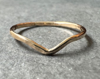 May include: A simple gold ring with a V-shaped design. The ring is made of a thin band of metal and has a smooth, polished finish.