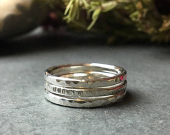 May include: A set of three silver stacking rings with hammered and textured finishes. The rings are stacked on top of each other and are shown on a gray surface.