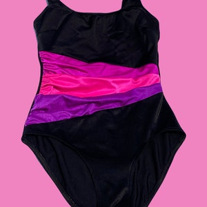 May include: A black swimsuit with a pink and purple striped design. The swimsuit has a scoop neck and thin straps.