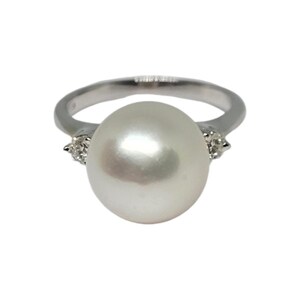 May include: A silver ring with a large white pearl and two smaller diamonds on either side.