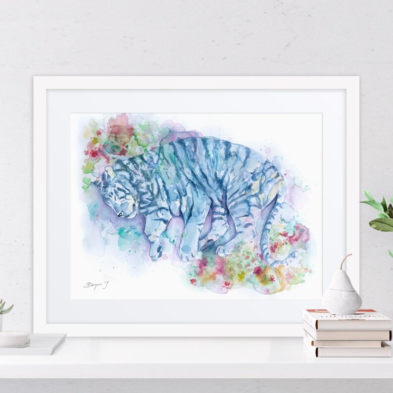 a framed watercolor painting of a tiger, with a white frame and a white shelf below it.