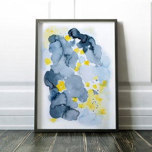 May include: Abstract watercolor art print in a black frame. The artwork features blue and gray cloud-like shapes with yellow floral accents on a white background. The framed art is displayed on a dark wooden floor.