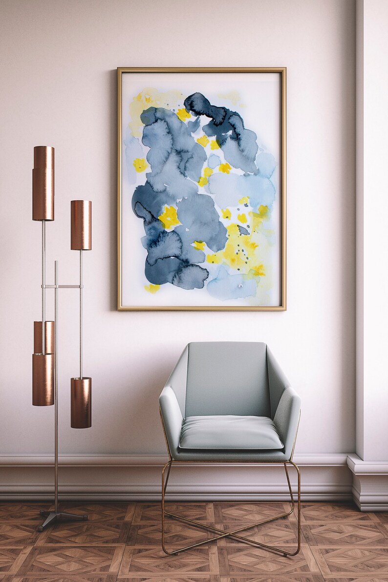 May include: An abstract watercolor painting in a gold frame, featuring blue, yellow, and dark blue shapes. A light blue armchair with a gold frame sits below the artwork. A modern floor lamp with copper shades is to the left.