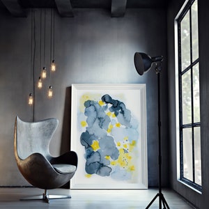 May include: An interior design scene featuring a gray leather egg chair, a framed abstract watercolor painting with blue and yellow hues, and a black floor lamp. Edison bulb pendant lights hang from the ceiling, and a large window is visible.