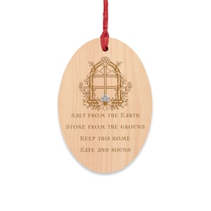 Może przedstawiać: Owalna drewniana ozdoba z czerwoną wstążką do zawieszenia. Ozdoba posiada dekoracyjny wzór okna z kwiatowymi akcentami oraz słowa "Salt From The Earth, Stone From The Ground, Keep This Home Safe And Sound."
