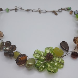 May include: A green and brown beaded necklace with a floral design. The necklace is made of wire and features various glass beads, including green, brown, and clear.