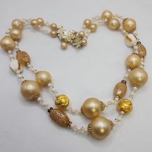 May include: A double strand necklace with large gold and white beads. The necklace has a gold leaf charm.