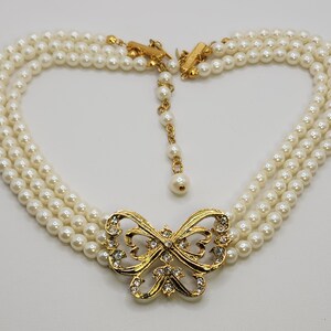 May include: A gold tone necklace with a butterfly pendant featuring clear rhinestones. The necklace is made of three strands of faux pearls.