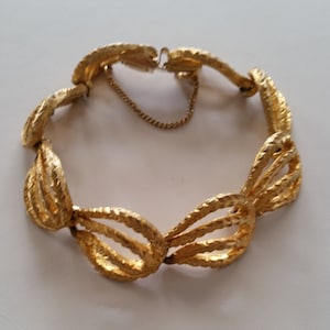 May include: A gold-toned bracelet with a textured, woven design. The bracelet is made of metal and has a clasp closure.