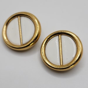 May include: A pair of gold-tone earrings with white enamel circles. Each circle has a vertical line down the center.