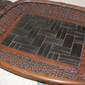 May include: A wooden tray with a woven black and brown bamboo design. The tray has two carved wooden handles.