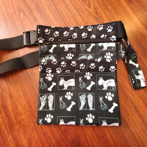 May include: Black fabric waist bag with a paw print and x-ray pattern. The bag has two zippered compartments and an adjustable strap. The bag has a label that says "Dog Treat".