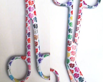 May include: A pair of white bandage scissors with a colorful paw print pattern. The scissors have a curved blade and a spring-loaded handle.