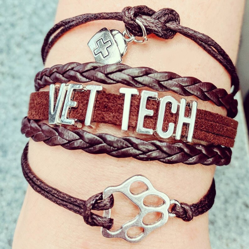 Op de afbeelding: Bruin leren armbandset met een zilveren bedel met de tekst "VET TECH" en een bedel in de vorm van een poot.