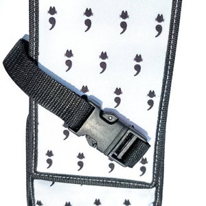May include: A white canvas pouch with a black adjustable strap and a black plastic buckle. The pouch has a repeating pattern of black semicolon symbols.