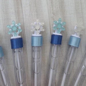 May include: Six clear bubble wands with snowflake toppers. The wands have blue and light blue ribbon accents. The snowflake toppers are white and light blue.
