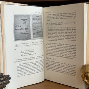 K&ouml;nnte beinhalten: Ein offenes Buch mit gealterten, vergilbten Seiten. Die linke Seite zeigt ein gedrucktes Bild mit deutschem Text. Die rechte Seite enth&auml;lt gedruckten Text. Ein dekorativer goldfarbener Bison-Buchst&uuml;tze ist sichtbar.