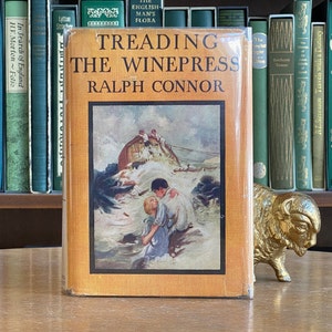 May include: A vintage hardcover book titled "Treading the Winepress" by Ralph Connor. The book cover features an illustration of a ship in a stormy sea with a man and woman clinging to each other.