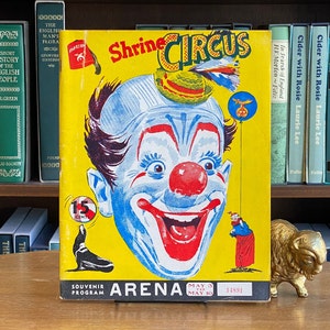 May include: A yellow and red Shrine Circus souvenir program featuring a smiling clown with a red nose and a blue face. The program advertises the circus at the Arena from May 3rd to May 10th. The program costs 15 cents.