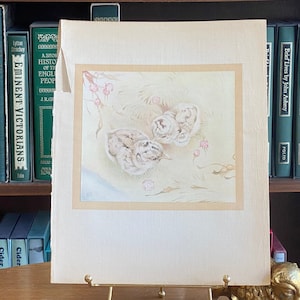 May include: A vintage illustration of two baby birds nestled in a nest of grass and flowers. The birds are depicted in a soft, watercolour style with delicate details. The illustration is framed in a cream-coloured mount and has a light brown border.
