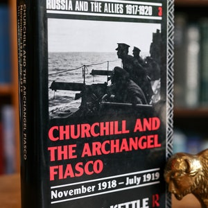 Puede incluir: Un libro de tapa dura negro titulado "Churchill y el fiasco de Archangel" de Michael Kettle. La portada del libro presenta una foto en blanco y negro de soldados en un barco con una ametralladora. El libro forma parte de una serie titulada "Rusia y los Aliados 1917-1920".