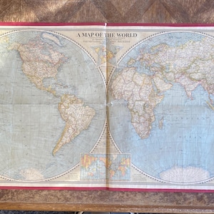 May include: A vintage world map printed on paper with a red border. The map is titled "A Map of the World" and includes the text "The National Geographic Magazine".