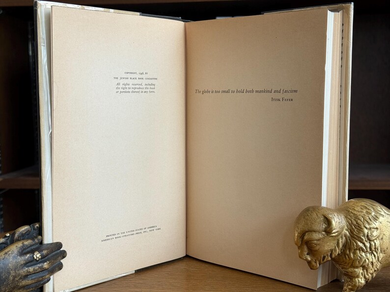 K&ouml;nnte beinhalten: Ein aufgeschlagenes Buch mit beigefarbenen Seiten, auf denen Text gedruckt ist. Auf der rechten Seite befindet sich eine goldfarbene Bison-Statue. Der Buchr&uuml;cken ist sichtbar, und die Seiten wirken leicht gealtert.