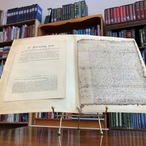 May include: A close-up of a historical document displayed on a metal stand. The document is yellowed and has handwritten text in black ink. The document is titled "A Fascinating Relic" and includes a transcription of the text. The document is surrounded by bookshelves filled with books.
