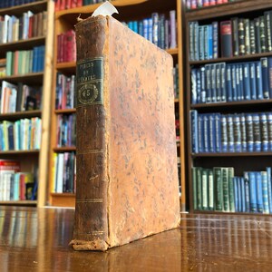 Könnte beinhalten: Ein antikes, braunes, ledergebundenes Buch mit goldenen Verzierungen und dem Titel "Pieces de Theatre" auf dem Rücken. Das Buch liegt auf einer Holzoberfläche.