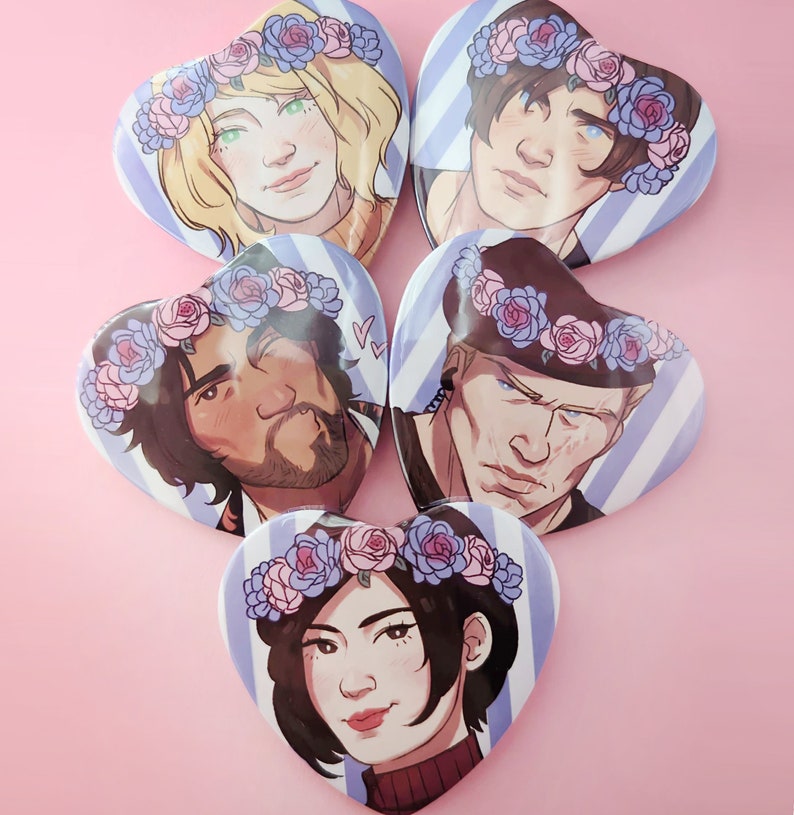 May include: Five heart-shaped buttons with blue and white stripes. Each button features a different illustration of a person with a floral crown. The crowns are pink and blue with white flowers.