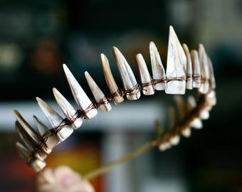 May include: A crown featuring a series of pointed, iridescent, off-white shell fragments arranged in a row. Each individual shell piece is securely attached to a thin, flexible metal wire frame using dark brown wire wrapping techniques.