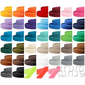 Könnte beinhalten: Eine Sammlung farbenfroher Klettbandrollen in verschiedenen Farbtönen, darunter Gelb, Orange, Rot, Rosa, Lila, Blau, Grün, Braun, Grau, Schwarz und Weiß. Die Rollen sind gestapelt und zeigen die verschiedenen verfügbaren Farben.