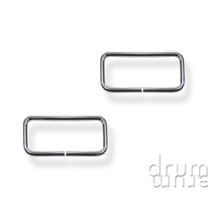 Könnte beinhalten: Zwei silberfarbene rechteckige Metallringe, jeweils mit einer kleinen Lücke. Die Ringe sind 2,5 cm groß. Der Hintergrund ist schlicht weiß.