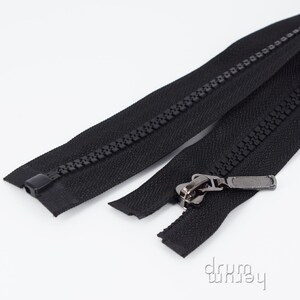Könnte beinhalten: Zwei schwarze Reißverschlüsse vor weißem Hintergrund. Einer ist geschlossen, der andere teilweise geöffnet und zeigt den Metall-Zipper. Diese strapazierfähigen Reißverschlüsse eignen sich für verschiedene Nähprojekte und bestehen aus robustem Material.