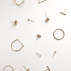 May include: A collection of gold-toned earrings, including a variety of shapes and styles, such as circles, bars, and studs. The earrings are displayed on a white background.