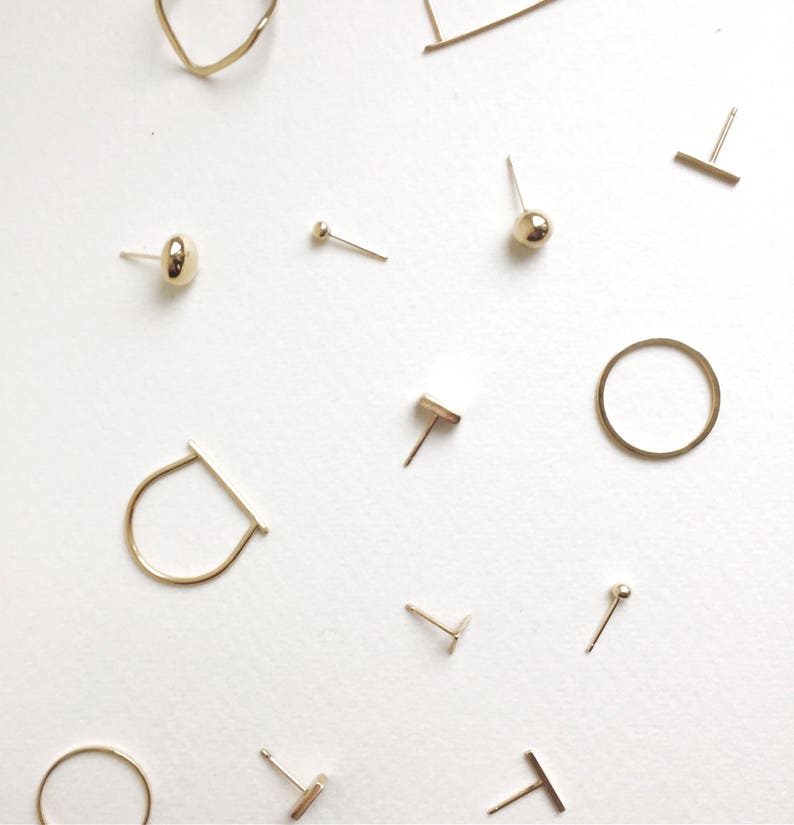 May include: A collection of gold-toned earrings, including a variety of shapes and styles, such as circles, bars, and studs. The earrings are displayed on a white background.