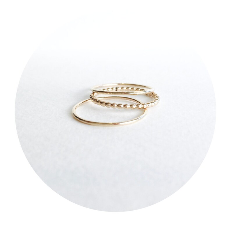 May include: Three gold stacking rings. The top ring is a beaded ring, the middle ring is a plain band, and the bottom ring is a plain band.
