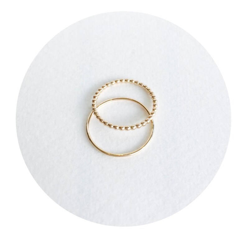 May include: Two gold rings, one with a beaded design and the other a simple band, are stacked on top of each other.