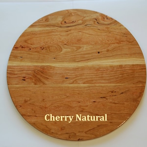 May include: A round wooden tabletop with a natural cherry finish. The wood grain is visible, and the surface is smooth. The text "Cherry Natural" is printed in gold. This table is suitable for various home decor styles.