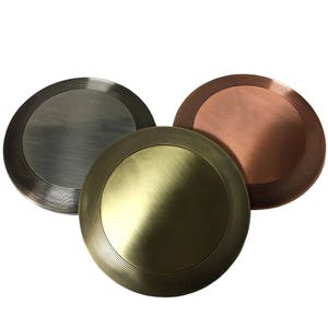 Può includere: Tre medaglioni rotondi in metallo con un bordo rialzato e cerchi concentrici. I medaglioni sono argentati, dorati e bronzo.